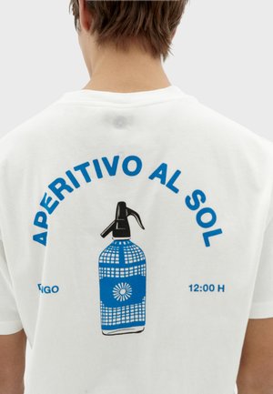Biela tričko s modrou grafikou rozprašovača. Text znie: „APERITIVO AL SOL“ v tučných modrých písmenách nad a pod fľaškou.