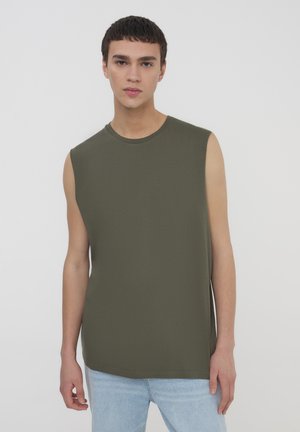 Top verde in cotone senza maniche con scollo rotondo, taglio dritto e texture morbida, abbinato a jeans in denim blu chiaro.