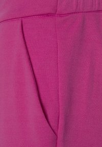 Fuchsia fabric close-up featuring smooth texture, structured seams, and a side pocket detail. Soft and stretchy material.
