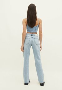 Top corto de mezclilla azul claro y jeans de cintura alta. Textura suave, diseño ajustado con bolsillos traseros y dobladillo deshilachado en los jeans.