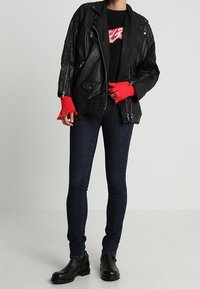 Chaqueta de cuero negra de biker con cremalleras gruesas, combinada con un suéter negro con un diseño rojo, jeans ajustados de mezclilla oscura y botas negras hasta el tobillo.