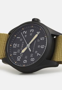 Schwarze, solarbetriebene Uhr mit dunklem Zifferblatt, weißen Stundenmarkierungen und gelben Akzenten. Verfügt über ein strapazierfähiges olivgrünes Stoffarmband.