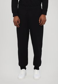 Sorte sweatpants lavet af blød stof, med elastisk talje og manchetter, parret med hvide sneakers. Enkel, lige ben design.