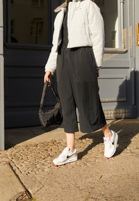 Vit vadderad jacka, svarta korta byxor, vita och svarta sneakers med röda accenter, samt en liten svart väska. Texturerade ytor och avslappnad passform.