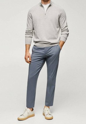 Pull gris clair à col zippé, pantalon bleu effilé et baskets blanches avec des accents beiges. Texture douce, design décontracté et coupe ajustée.