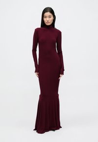 Bordó hosszú ujjú, testhezálló ruha magas nyakú kialakítással és bővülő szegéllyel, sima, rugalmas anyagból készült. Nincs rajta további minta vagy díszítések.