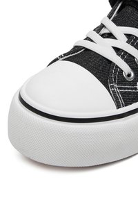 Juodas drobinis kedas su balta gumine pirštų srities apsauga ir padu, ryškiai kontrastuojančiomis siūlėmis ir baltais raišteliais ant grūdėto viršaus.