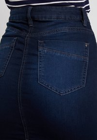 Tmavě modré vysoké džíny mají přiléhavou siluetu, klasický pětikapsový design a kontrastní švy podél kapes.