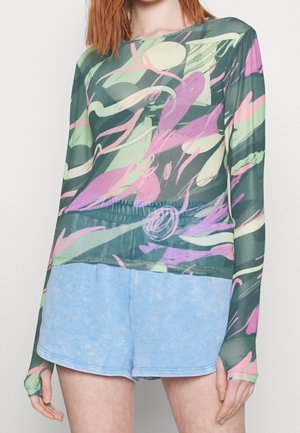 Green long-sleeve top with abstract pink and mint patterns, paired with light blue shorts. The top features a relaxed fit and textured fabric.