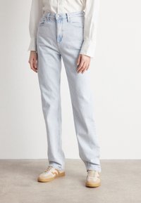 Ljusblå denimjeans med hög midja och rak passform, med subtil slitning. Bärs med tanfärgade och krämfärgade sneakers.