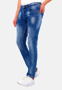 Blauwe skinny jeans van denim met een verweerd ontwerp, vijf zakken en een gladde textuur, gecombineerd met witte sportschoenen.