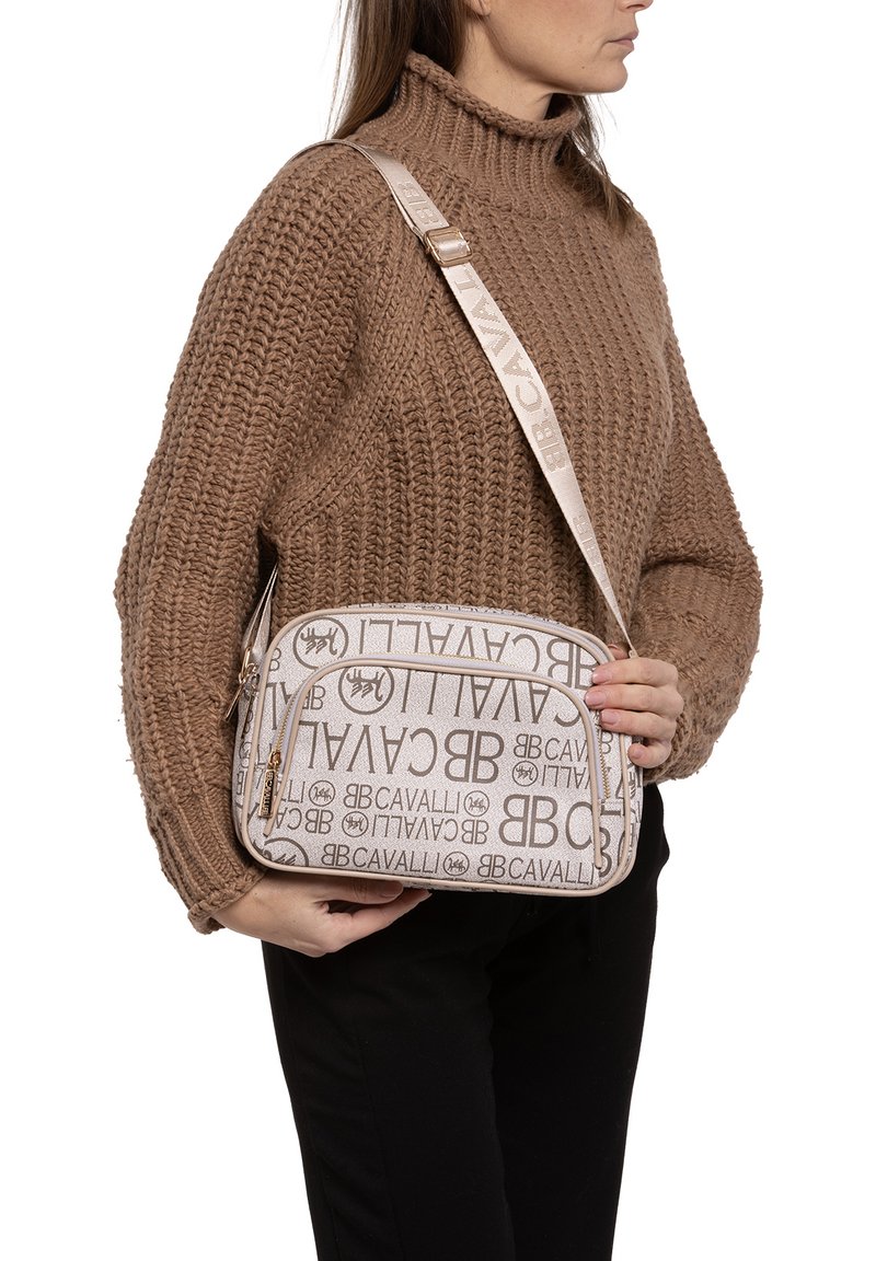 Borsa beige con motivo a logo in rilievo e dettagli dorati. Presenta un design curvo e una tracolla regolabile. Il tessuto testurizzato dona profondità.
