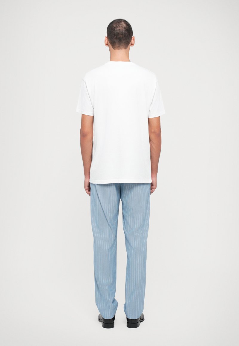 White cotton t-shirt with short sleeves, paired with light blue pinstriped pants, standing on a plain background.