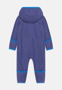 Lila fleeceoverall med huva. Har blå accentdetaljer längs ärmslut och krage. Mjuk textur, heltäckande design och inga knäppningar.