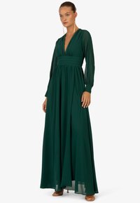 Ein langes grünes Kleid aus fließendem Stoff, mit einem tiefen V-Ausschnitt, plissiertem Bund und langen, transparenten Ärmeln. Glatte Textur mit einer definierten Silhouette.