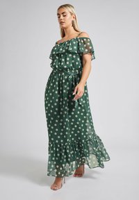 Vihreä pilkullinen maksimekko, jossa on rypytetty pois olkapäältä -design, säädettävät henkselit, nyöritetty vyötärö ja kerroksellinen helma. Läpikuultavaa, kevyttä kangasta.