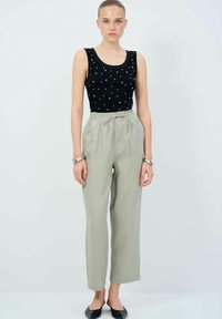 Černý top na ramínka s bílými tečkami, v kombinaci s volnými světle šedými kalhotami s elastickým pasem a rovnými nohavicemi. Outfitu dominují černé boty.