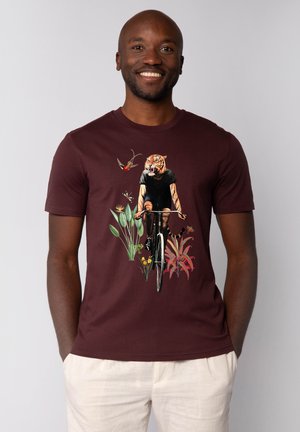 Bordeaux kleurig t-shirt met korte mouwen, versierd met een afbeelding van een tijger op een fiets, omringd door planten en vogels. Gladde katoenen stof, casual pasvorm.