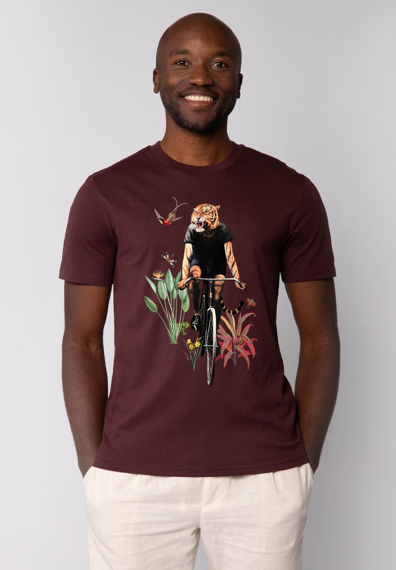 Bordeaux kleurig t-shirt met korte mouwen, versierd met een afbeelding van een tijger op een fiets, omringd door planten en vogels. Gladde katoenen stof, casual pasvorm.