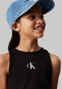 Top senza maniche nero con un logo "cK" bianco sul davanti; abbinato a un cappellino di jeans blu chiaro con visiera curva.