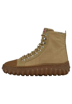 Υψηλό καφέ sneakers με χοντρή υφασμάτινη καφέ σόλα, μεταλλικά μάτια, κορδόνια και επενδεδυμένο κολάρο αστραγάλου, παρουσιασμένο από το πλάι σε λευκό φόντο.