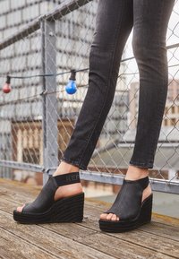 Sandalias cuña negras con parte superior texturizada y puntera abierta. Cuenta con una amplia correa elástica con "REP" y un patrón de suela similar a una cuerda.