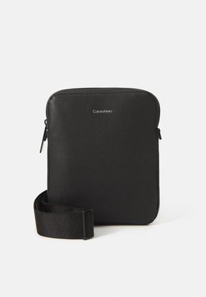 Sac compact noir en cuir texturé, doté d'une fermeture éclair, d'une bandoulière en tissu réglable et d'un logo argenté à l'avant.