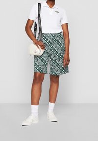 Vihreät, kuviolliset shortsit valkoisilla logoilla, yhdistettynä valkoiseen polo-paitaan. Lisänä pieni valkoinen olkalaukku ja valkoiset tennarit.