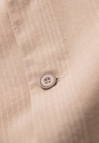 Tissu beige à texture côtelée verticale avec un petit bouton rond à quatre trous cousu près du centre.