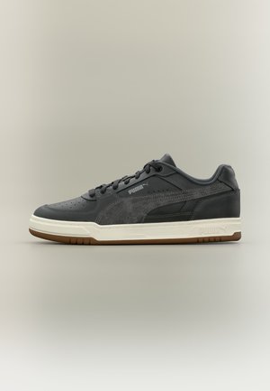 Baskets basses Puma noires avec semelle blanche et semelle extérieure en gomme, avec un détail en daim sur le côté et un laçage à l'avant.