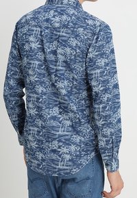 Langärmliges Hemd in Marineblau mit einem tropischen Muster aus Palmen und Blumen in hellblauen Tönen. Baumwollmaterial, entspannter Schnitt.