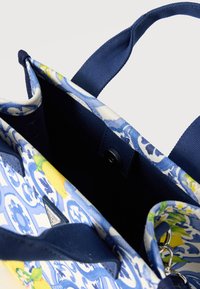 Ανοιχτή τσάντα ώμου με μπλε και λευκά φλοράλ σχέδια, κίτρινες λεπτομέρειες λεμονιού, μπλε χερούλια και μικρό εσωτερικό κλείσιμο με κουμπί.