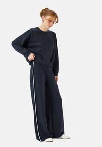 Marineblauwe oversized sweatshirt en wijdvallende joggingsbroek met witte zijstrepen. Zachte stof, casual pasvorm, ronde hals en geribbelde boorden.