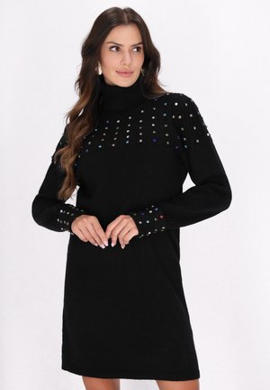 Schwarzes Strickkleid mit Rollkragen, verziert mit bunten Edelsteinakzenten an Schulter und Ärmeln. Weicher Stoff, schlichte Form, knielang.