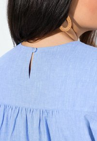 Blusa blu chiaro con scollatura tonda e chiusura a chiave, con dettagli arricciati in vita. Tessuto morbido.
