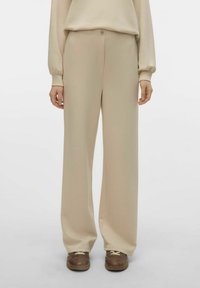 Pantaloni beige a gamba larga realizzati in tessuto morbido con una texture liscia, dotati di chiusura a bottone e elementi di design minimali.