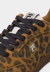 Αθλητικό παπούτσι με λεοπάρ σχέδιο, μαύρα κορδόνια, λευκή ετικέτα γλώσσας με λογότυπο της μάρκας και καφέ σόλα σε κοντινή προβολή.