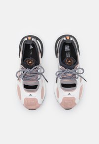 Chaussures de sport avec une tige en tricot respirante, rose et gris, avec des accents blancs, une doublure noire et des lacets ronds noirs. Détail de logo notable.