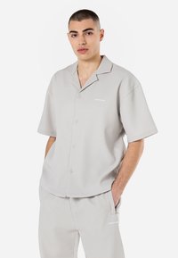 Camisa de botão de manga curta cinza claro com textura em reque. Possui colarinho com recorte, bolso frontal e logótipo discreto no peito.