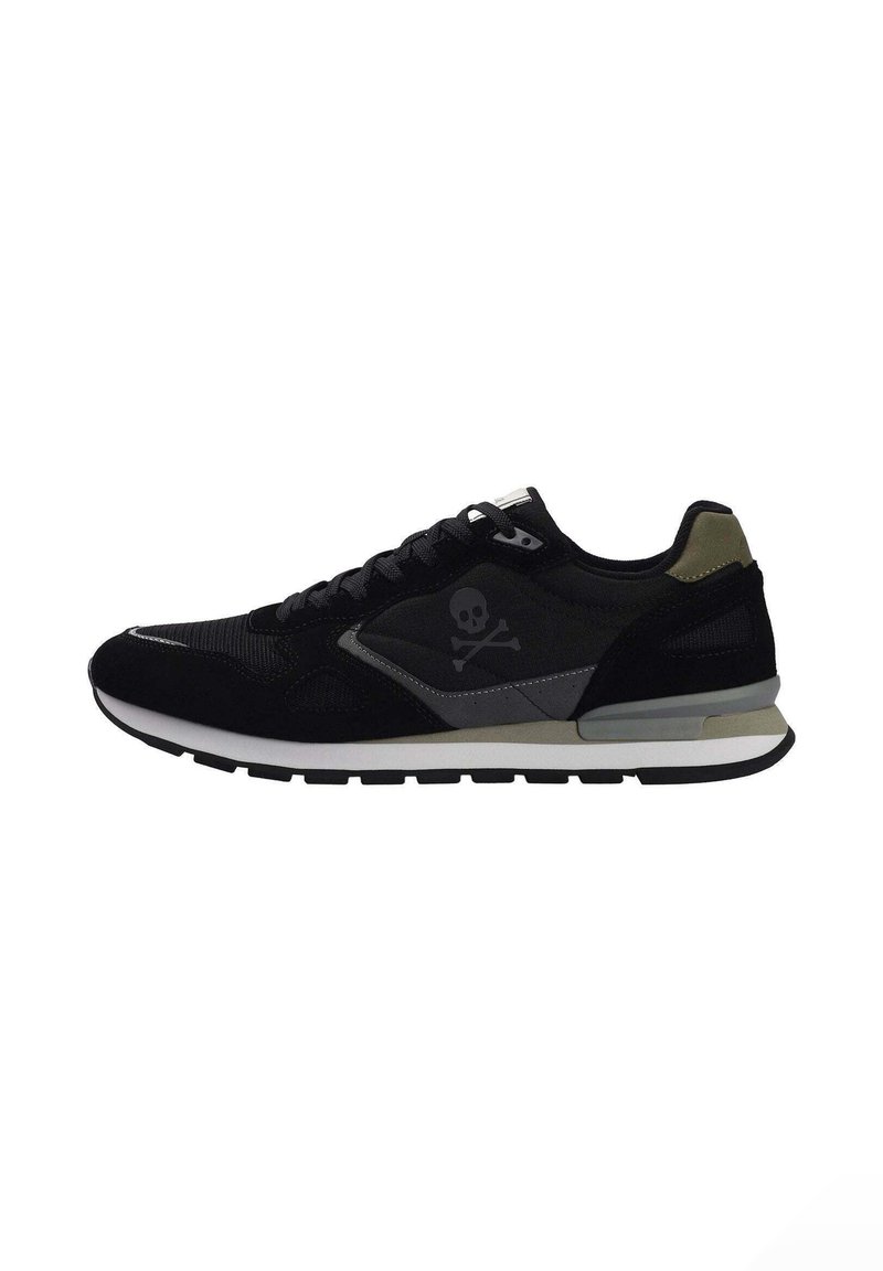 Zapatilla deportiva negra con parte superior de ante y malla, acentos en gris contrastante, logo de calavera y huesos cruzados, y suela blanca.