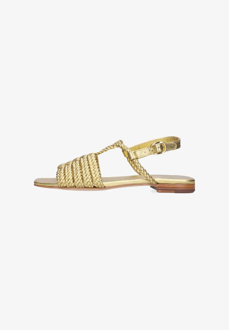 Goldene flache Sandale mit geflochtenen Riemen über dem Vorderfuß, einem geflochtenen T-Riemen und einer verstellbaren Schnalle am Knöchel auf einem niedrigen Holzabsatz.