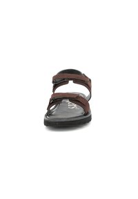 Sandale en cuir brun avec deux brides réglables, une semelle noire texturée et une semelle intérieure rembourrée, comportant des détails cousus et un design courbé.