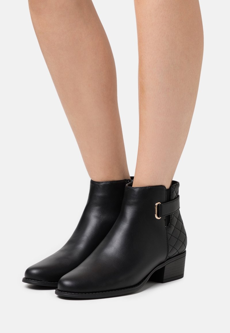 Botas negras hasta el tobillo con un acabado de cuero suave, panel trasero acolchado y hebilla en tono dorado. Punta cuadrada y tacón bajo.