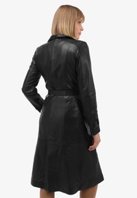 Zwarte leren trenchcoat met een ceintuur in de taille, kraag en lange mouwen, met een gladde textuur en stiksels op de achterkant.