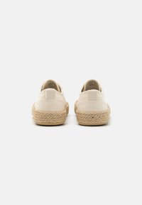 Zapatos de lona beige con un patrón texturizado, suelas de goma y acentos de yute trenzado alrededor del borde; diseño bajo con detalle en el tirador del talón.
