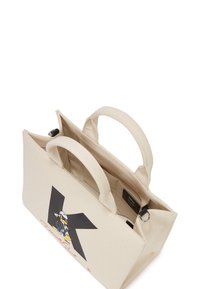 Sac fourre-tout en toile beige avec double poignée, arborant un logo 'K' noir et un graphique de personnage de dessin animé. Poche intérieure avec fermeture à glissière.