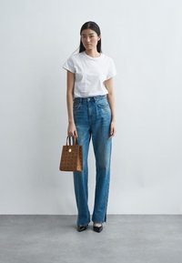 Hvid kortærmet t-shirt, blå højtaljede jeans, brun perforeret håndtaske med korte håndtag, og sorte spidse hæle.