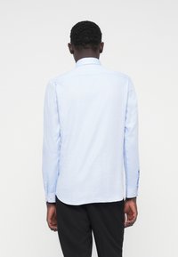 Γαλάζιο μακρυμάνικο πουκάμισο με ίσια κοπή, μανσέτες με κουμπιά και απαλό υλικό υφής. Χωρίς ορατά σχέδια. Πλάγια όψη από πίσω.