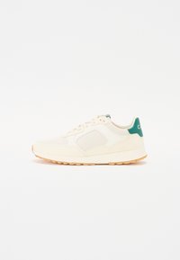 Cream-colored sneaker with mesh panels, a green accent heel, and a textured rubber sole. Laces in matching tone complete the design.