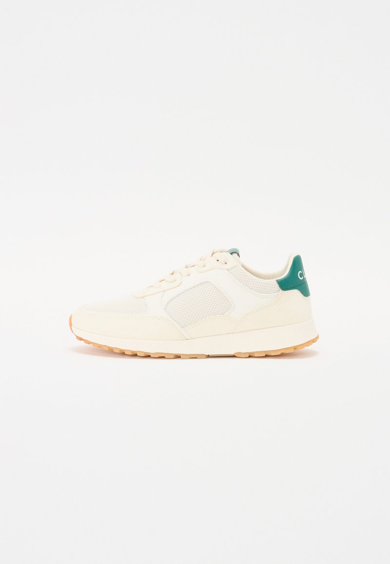 Cream-colored sneaker with mesh panels, a green accent heel, and a textured rubber sole. Laces in matching tone complete the design.